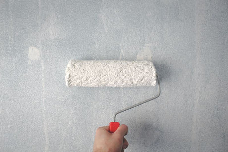 A person priming a wall with a roller.