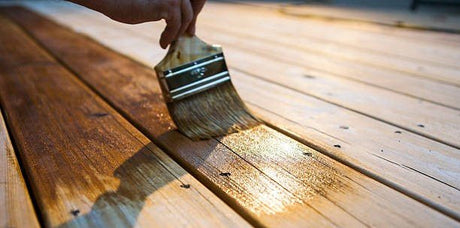 A person painting wood stain onto a deck.