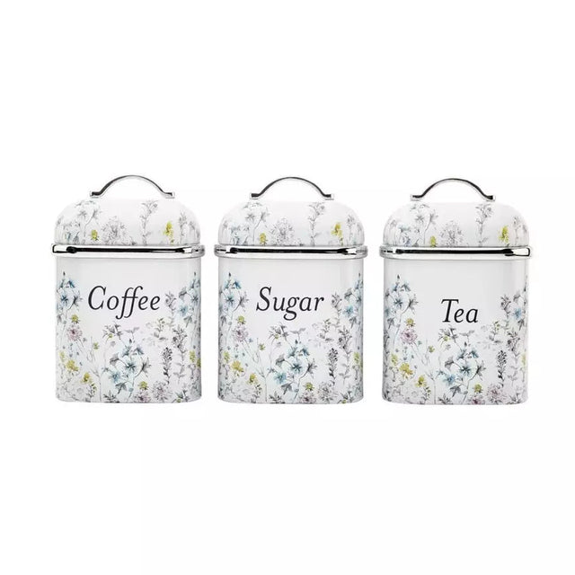 Three white enamel canisters with lids for coffee, sugar, and tea, decorated with a delicate blue and yellow floral pattern.