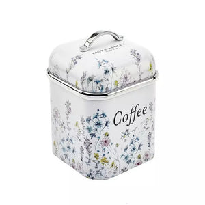 A square metal coffee canister with a hinged lid and top handle, decorated with a delicate blue, green, and yellow floral pattern on a white background. The word 'Coffee' is printed in black script on the front.